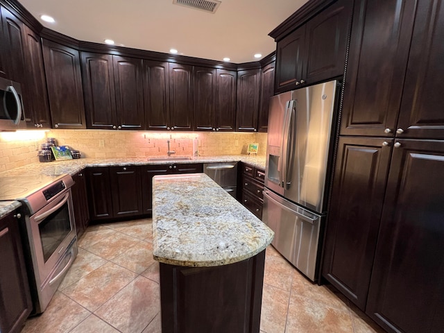 kitchen featuring sink, backsplash, light stone counters, dark brown cabinetry, and stainless steel appliances