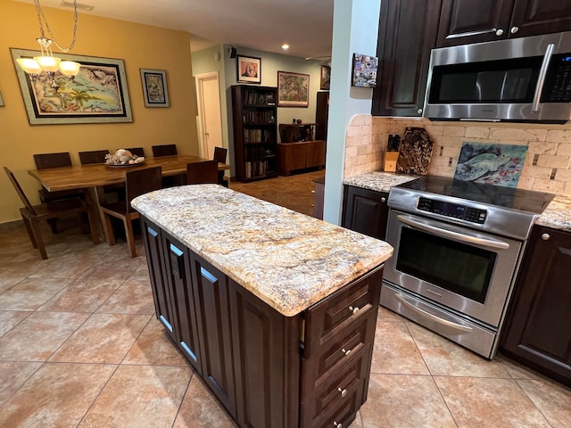 kitchen with appliances with stainless steel finishes, dark brown cabinets, light stone counters, decorative backsplash, and decorative light fixtures