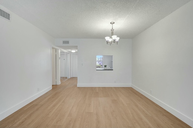 unfurnished room featuring a textured ceiling, light wood-type flooring, visible vents, and a notable chandelier