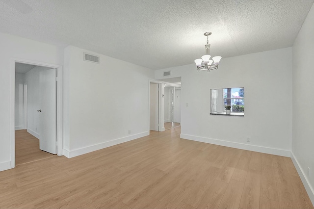 spare room with an inviting chandelier, light wood-style flooring, visible vents, and a textured ceiling