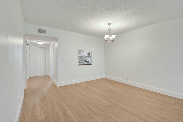 spare room with visible vents, an inviting chandelier, light wood-style floors, a textured ceiling, and baseboards