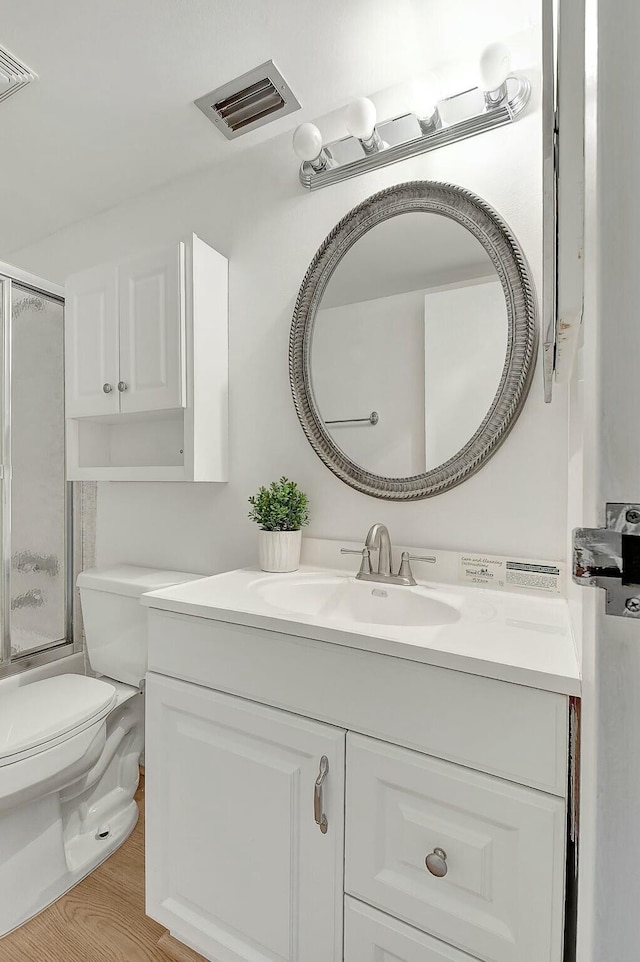 bathroom with toilet, enclosed tub / shower combo, visible vents, and vanity