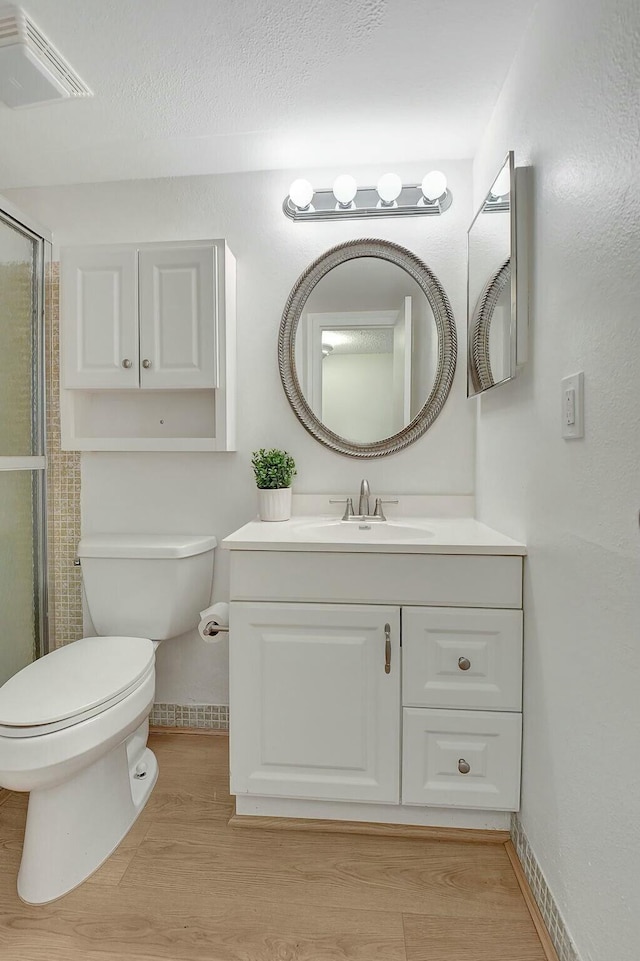 full bath with toilet, wood finished floors, vanity, visible vents, and a stall shower