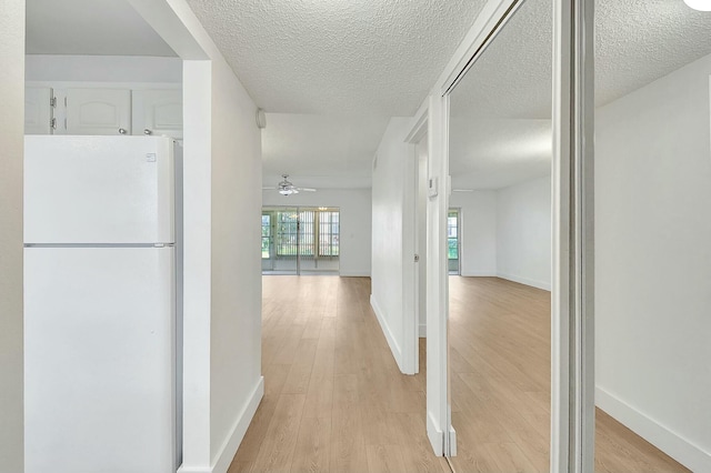 corridor featuring a textured ceiling, light wood-type flooring, and baseboards