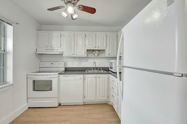 kitchen featuring white appliances, white cabinets, dark countertops, under cabinet range hood, and a sink