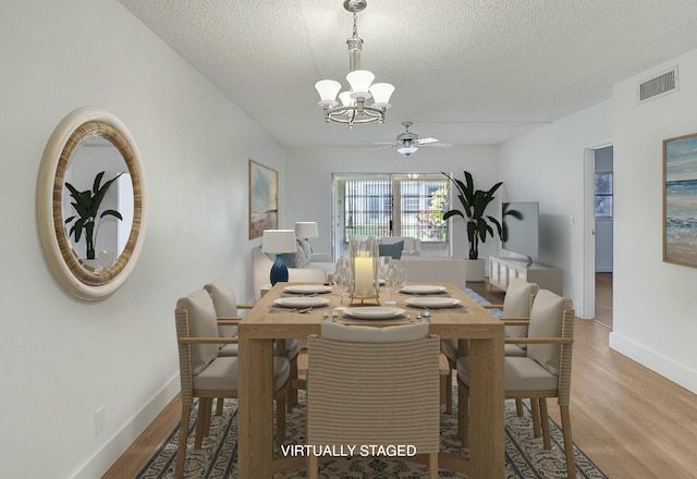 dining space featuring light wood-style flooring, visible vents, a textured ceiling, and ceiling fan with notable chandelier