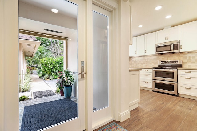 kitchen with tasteful backsplash, white cabinetry, light hardwood / wood-style flooring, and appliances with stainless steel finishes