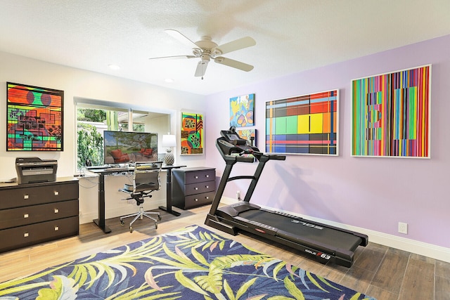 exercise room with a textured ceiling, light hardwood / wood-style floors, and ceiling fan