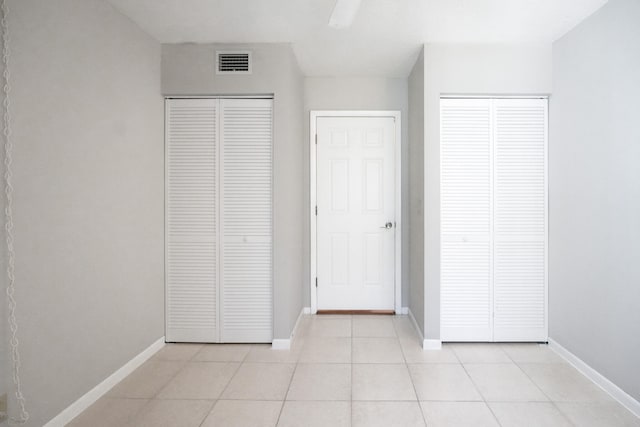 unfurnished bedroom featuring ceiling fan, light tile patterned floors, and two closets