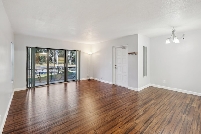 spare room featuring dark hardwood / wood-style flooring, a textured ceiling, and a notable chandelier