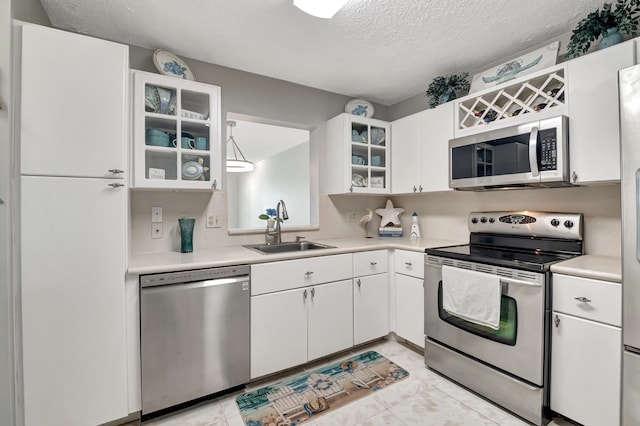 kitchen with sink, a textured ceiling, appliances with stainless steel finishes, light tile patterned flooring, and white cabinetry