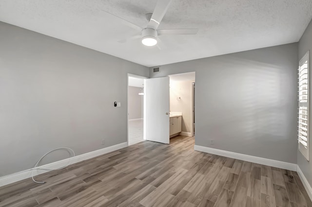 unfurnished bedroom featuring ceiling fan, wood-type flooring, a textured ceiling, and ensuite bath