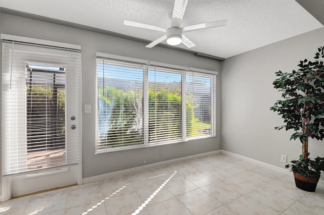 empty room with light tile patterned floors, a textured ceiling, plenty of natural light, and ceiling fan