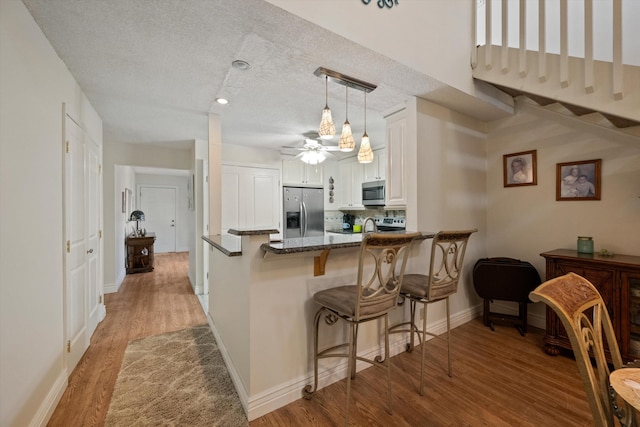 kitchen featuring a textured ceiling, stainless steel appliances, decorative light fixtures, light hardwood / wood-style flooring, and white cabinets