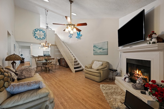 living room featuring ceiling fan with notable chandelier, light hardwood / wood-style floors, a textured ceiling, and high vaulted ceiling