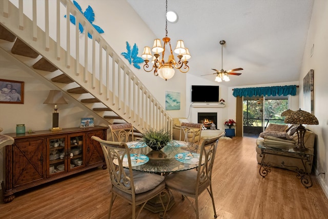 dining room with high vaulted ceiling, wood-type flooring, and ceiling fan with notable chandelier