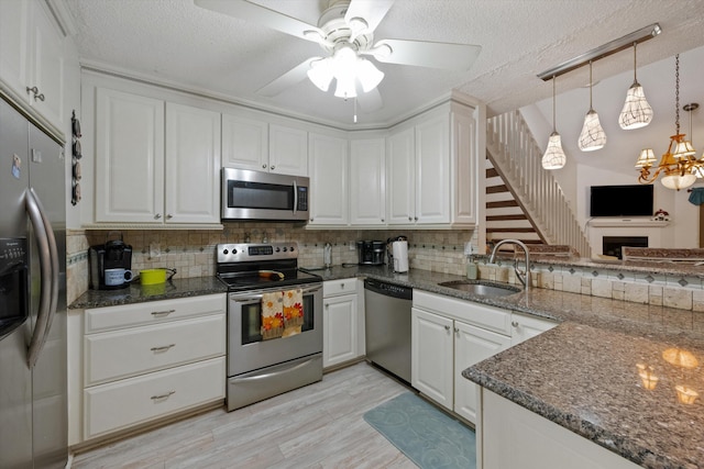 kitchen with sink, backsplash, stainless steel appliances, white cabinets, and decorative light fixtures