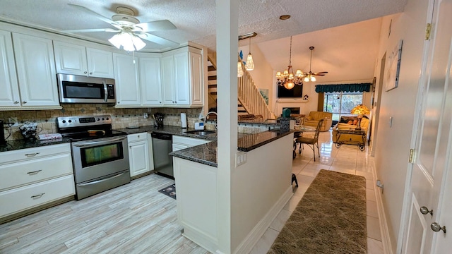 kitchen featuring tasteful backsplash, decorative light fixtures, stainless steel appliances, ceiling fan with notable chandelier, and white cabinets