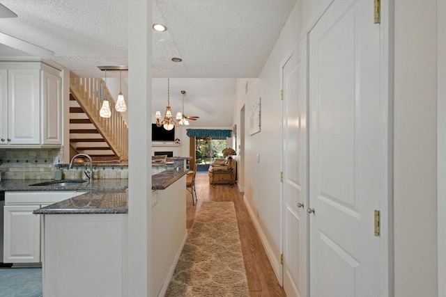 kitchen featuring a textured ceiling, sink, white cabinetry, and hanging light fixtures