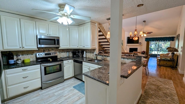 kitchen with appliances with stainless steel finishes, light wood-type flooring, sink, pendant lighting, and white cabinetry