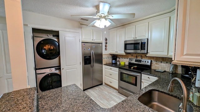 kitchen featuring dark stone countertops, sink, appliances with stainless steel finishes, and stacked washer and clothes dryer