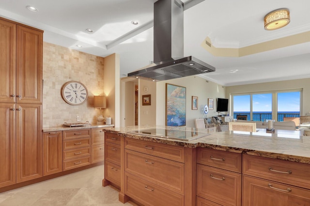 kitchen featuring light stone countertops, island exhaust hood, black electric cooktop, a tray ceiling, and ornamental molding