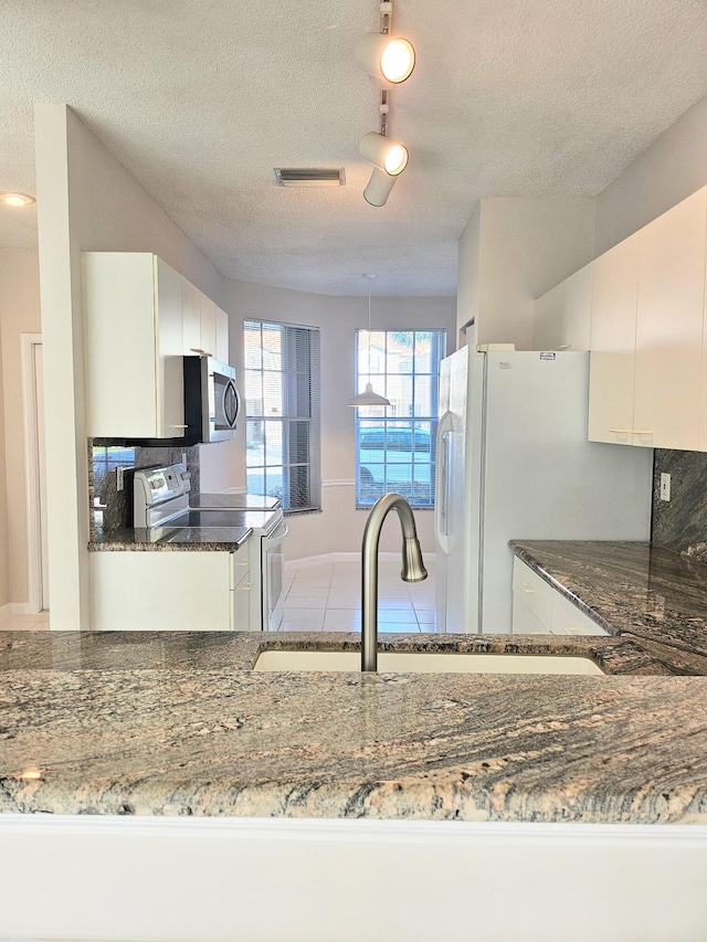 kitchen with white cabinets, a textured ceiling, appliances with stainless steel finishes, and dark stone counters