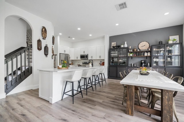 kitchen featuring backsplash, a kitchen breakfast bar, light wood-type flooring, appliances with stainless steel finishes, and white cabinetry