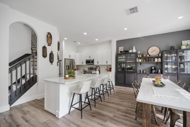 kitchen featuring stainless steel appliances, a kitchen breakfast bar, backsplash, white cabinets, and light wood-type flooring