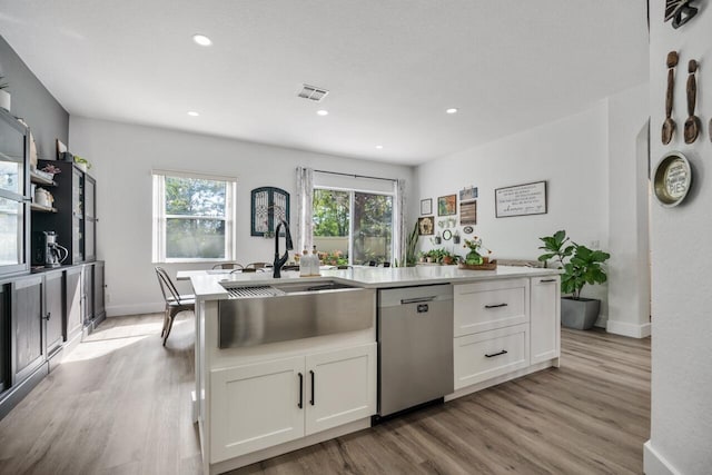 kitchen featuring white cabinets, sink, stainless steel dishwasher, an island with sink, and light hardwood / wood-style floors