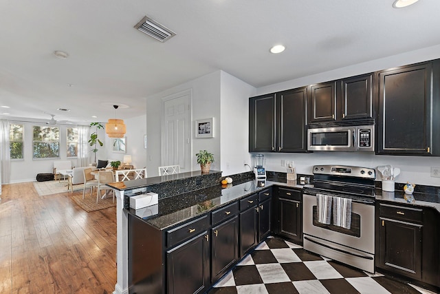 kitchen with hanging light fixtures, dark stone countertops, light wood-type flooring, kitchen peninsula, and stainless steel appliances