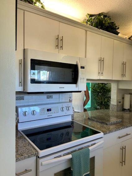 kitchen featuring a textured ceiling, dark stone countertops, white cabinets, and white appliances