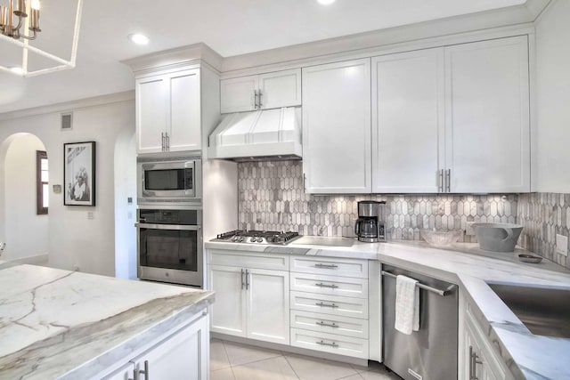 kitchen featuring tasteful backsplash, white cabinets, appliances with stainless steel finishes, light tile patterned flooring, and custom exhaust hood