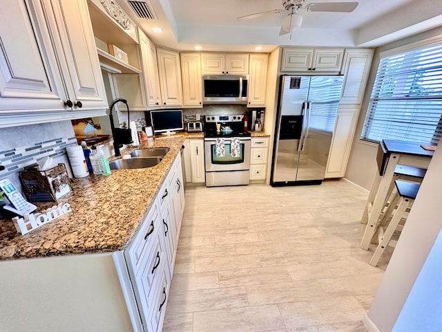 kitchen featuring sink, ceiling fan, light stone countertops, appliances with stainless steel finishes, and tasteful backsplash