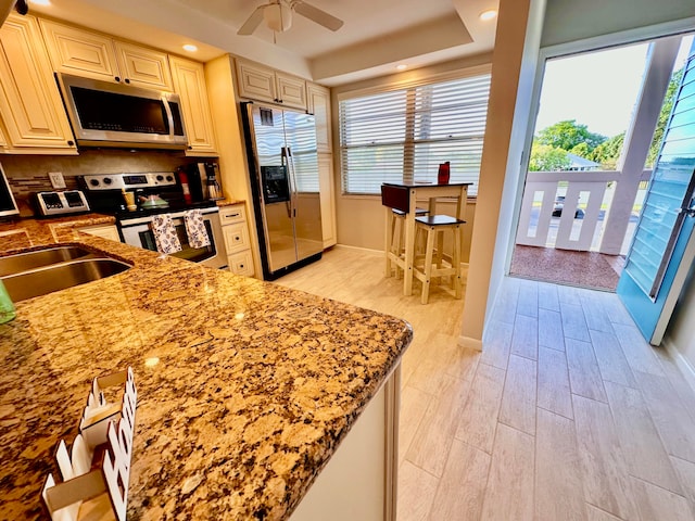 kitchen with appliances with stainless steel finishes, light wood-type flooring, light stone counters, ceiling fan, and cream cabinetry