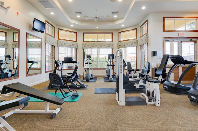 exercise room with a high ceiling, light colored carpet, ceiling fan, and a tray ceiling