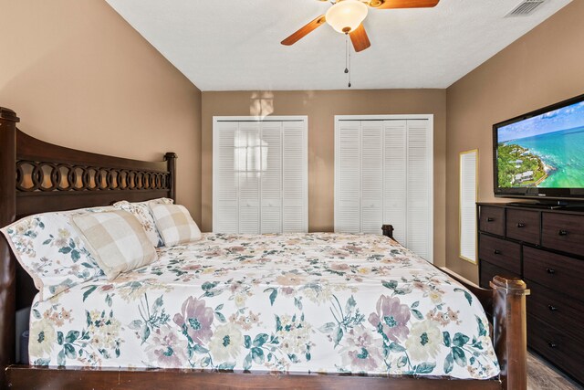 bedroom with a textured ceiling, ceiling fan, and two closets