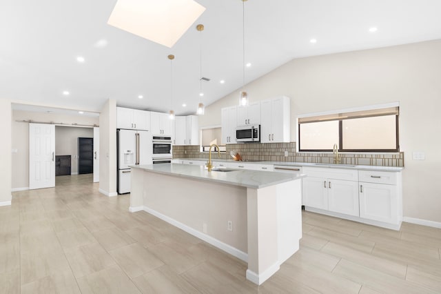 kitchen featuring sink, a barn door, a kitchen island with sink, white cabinets, and appliances with stainless steel finishes