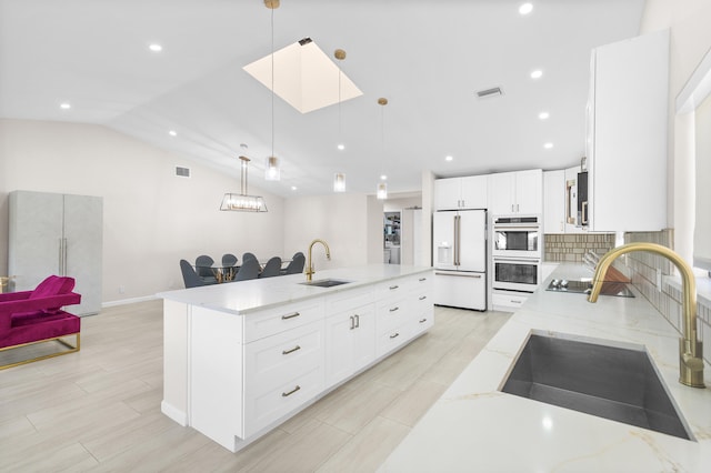 kitchen featuring white refrigerator with ice dispenser, sink, decorative light fixtures, light stone countertops, and a large island