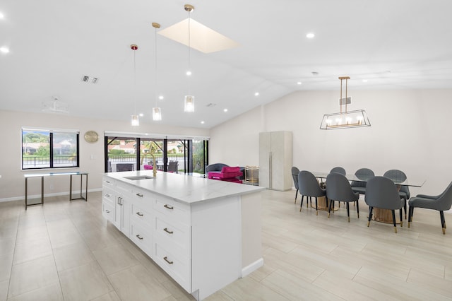 kitchen with light stone counters, pendant lighting, lofted ceiling, a kitchen island with sink, and white cabinets