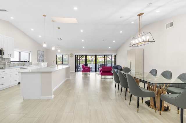 kitchen featuring a kitchen island with sink, sink, tasteful backsplash, decorative light fixtures, and white cabinetry