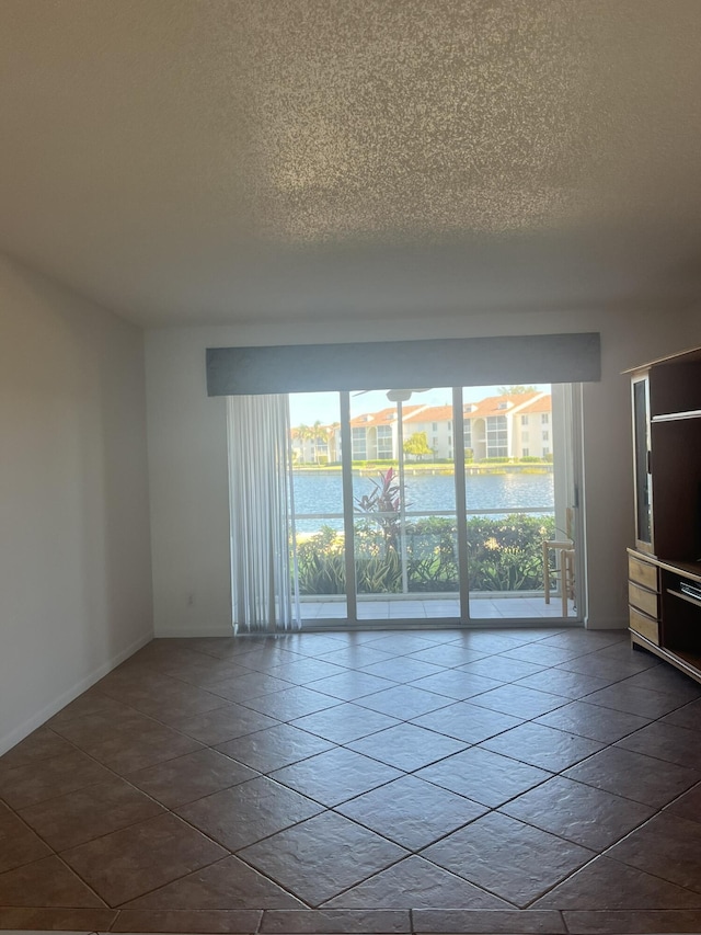 empty room with tile patterned flooring, a water view, and a textured ceiling