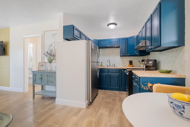 kitchen with tasteful backsplash, black range with electric cooktop, blue cabinetry, butcher block countertops, and stainless steel refrigerator