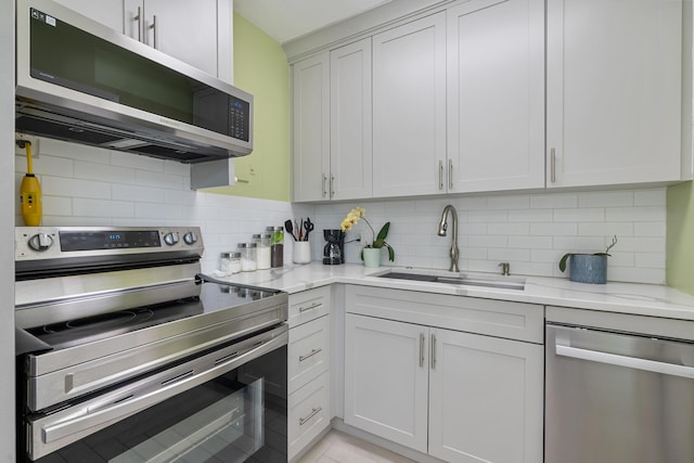 kitchen with sink, decorative backsplash, light stone countertops, appliances with stainless steel finishes, and white cabinetry