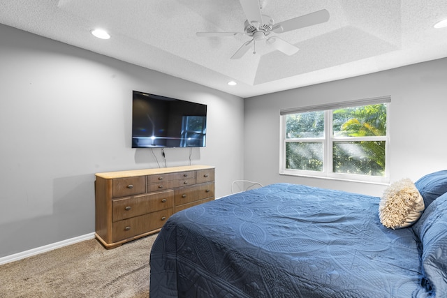 bedroom with a textured ceiling, ceiling fan, a tray ceiling, and light colored carpet