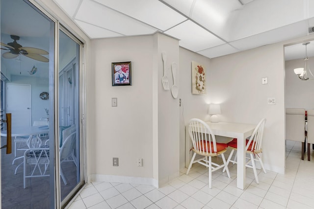 tiled dining room featuring ceiling fan with notable chandelier and a drop ceiling