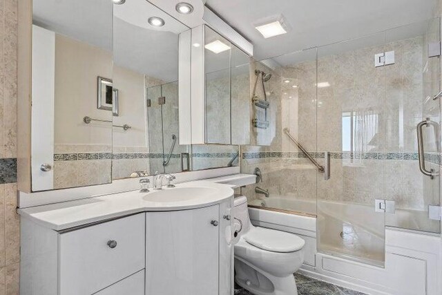 full bathroom with vanity, toilet, tile walls, and enclosed tub / shower combo