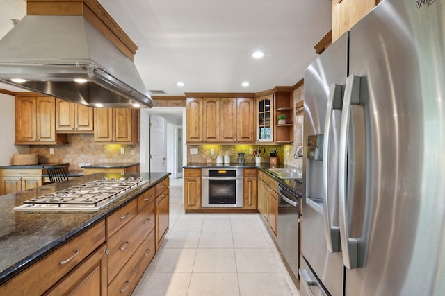 kitchen with sink, backsplash, dark stone counters, island range hood, and appliances with stainless steel finishes