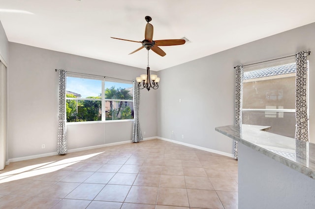 tiled spare room with ceiling fan with notable chandelier