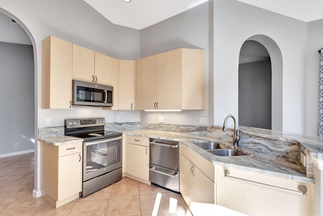 kitchen with kitchen peninsula, light stone countertops, appliances with stainless steel finishes, light tile patterned flooring, and sink